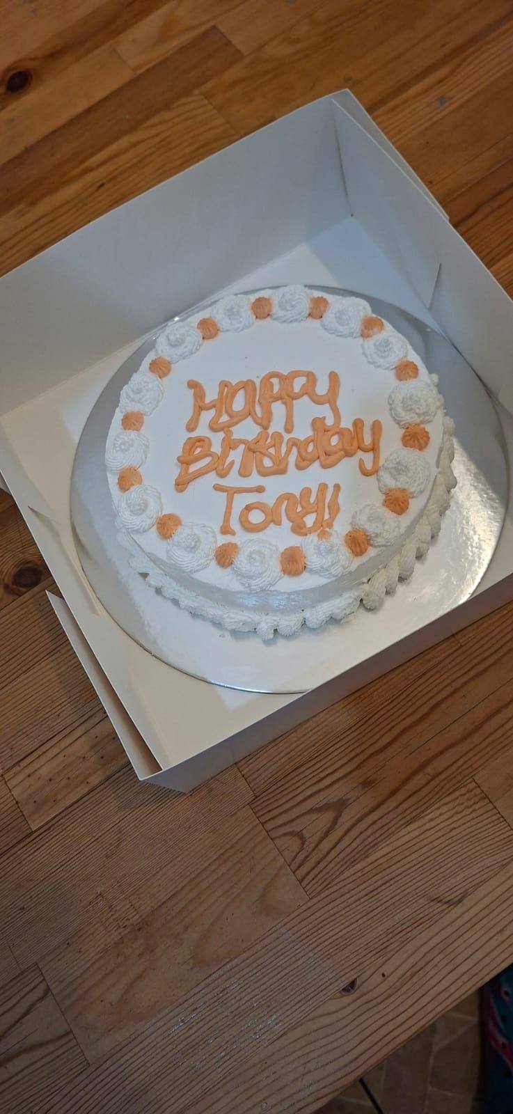 White cake in a box with a birthday message piped in orange icing