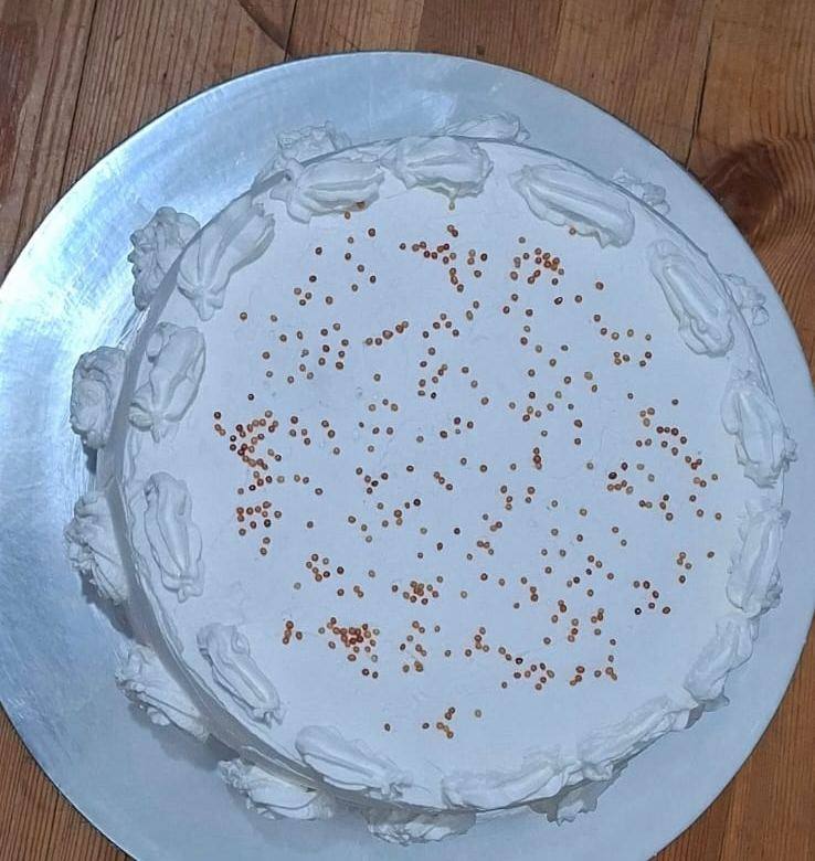 White cream cake with copper sprinkles and a piped shell border
