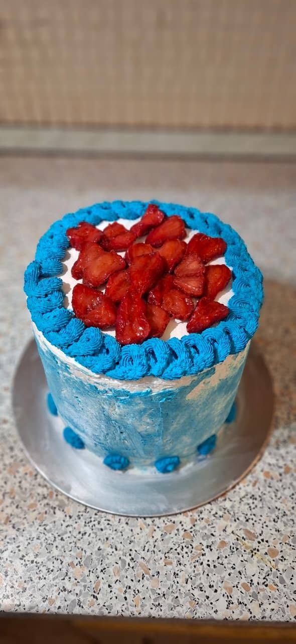 Blue cake topped with glazed strawberries inside a piped rope border