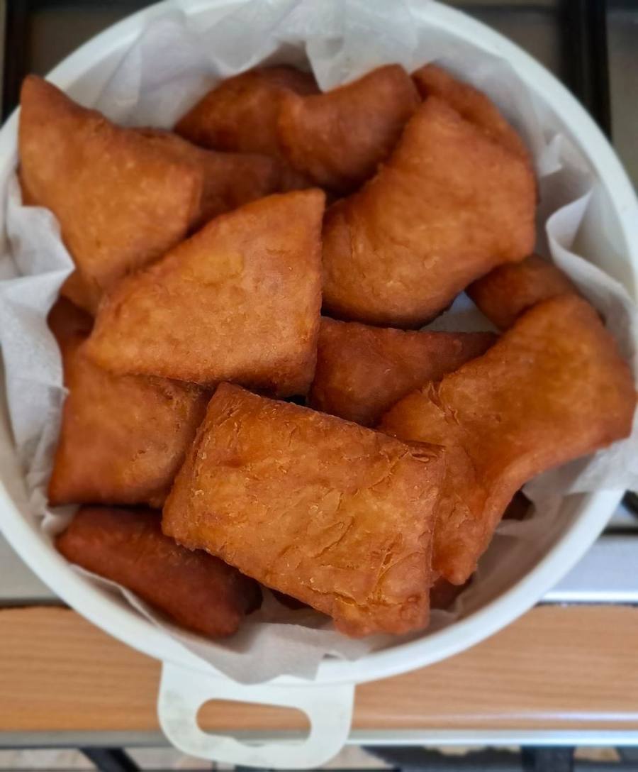 Freshly fried mandazi piled on a plate beside a cup of milky Kenyan tea